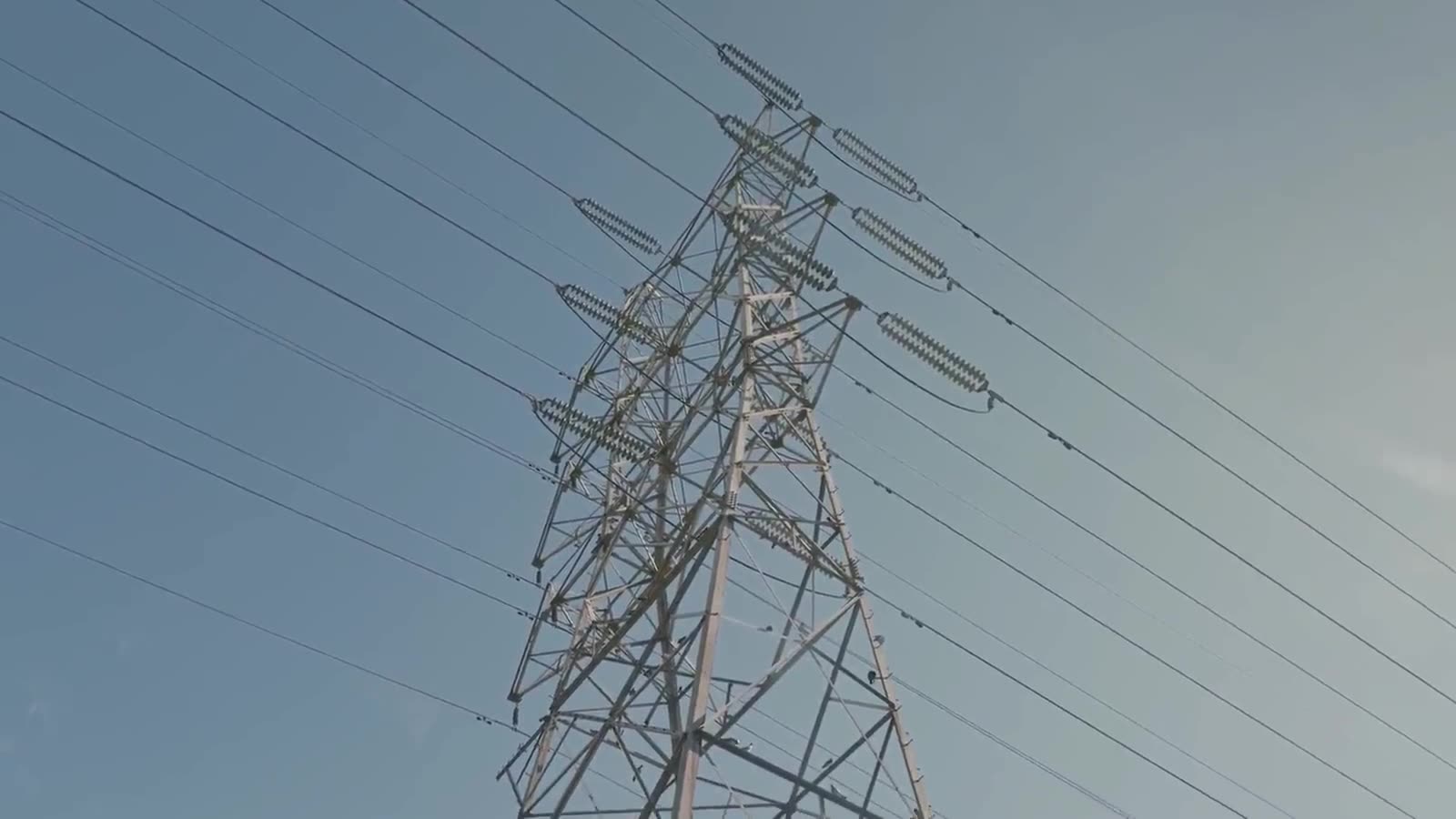 A high-voltage transmission tower carrying conductors across an open sky